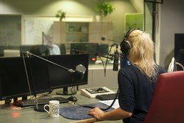 Radiomoderatorin in einem Radiostudio bei der Arbeit, mit dem Rücken zur/zum Betrachtenden