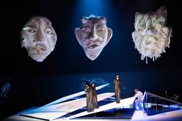 "Achill unter den Mädchen", KHP, Odysseus (Isaac Tolley) halb sitzend unter einer Bühnenrampe, in der Mitte die drei Frauen in schwarz, die drei Masken leuchten darüber